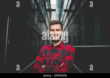 Sorridente uomo caucasico in flanella con braccia incrociate contro un edificio Foto Stock