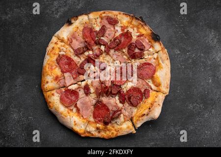 Quattro pizze di carne con carne, salsiccia, prosciutto e pollo su fondo di cemento scuro Foto Stock