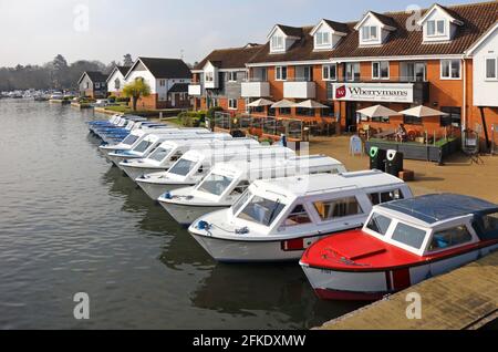 Una fila di barche ormeggiate noleggio giorno sul fiume Bure sul Norfolk Broads visto da Wroxham Bridge, Wroxham, Norfolk, Inghilterra, Regno Unito. Foto Stock