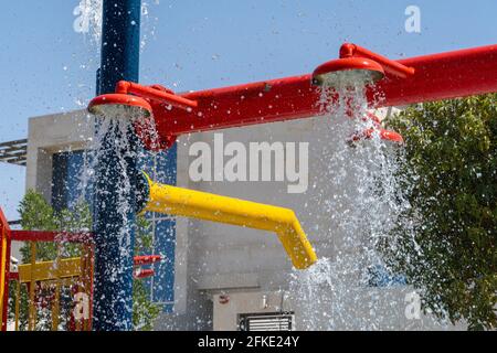 Tre sprinkler rossi del parco acquatico che spruzzano acqua sotto per il divertimento estivo dei bambini. Foto Stock