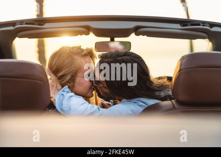 Felice coppia baciando in auto convertibile - persone romantiche che hanno momento tenero durante il viaggio su strada in città tropicale Foto Stock