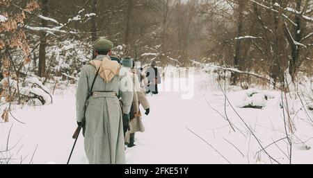 Uomini vestiti come soldati della Guardia Bianca dell'esercito imperiale russo nel tempo della Guerra civile russa che marchano attraverso la Foresta invernale innevata. Rievocazione storica Foto Stock