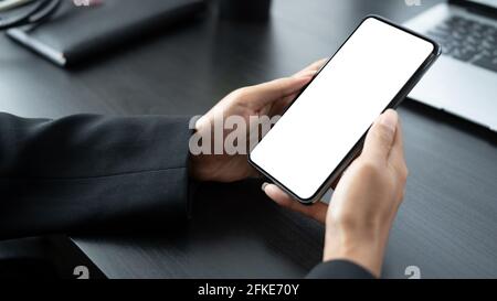 Immagine simulata di uomo d'affari che tiene il telefono cellulare con schermo vuoto su tavolo di legno nero. Foto Stock