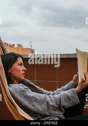 Giovane bruna ragazza che legge un libro in un amaca Foto Stock