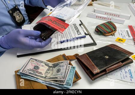 Un ufficiale di polizia specializzato prende il portafoglio con denaro da un sacchetto di prove di omicidio, immagine concettuale Foto Stock