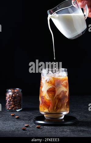Latte Versato In Caffè Freddo In Tall Glass Su Sfondo Scuro. Concept Drink Estivo Rinfrescante. Foto Stock