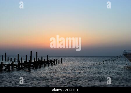 Mattina presto pochi minuti prima dell'alba. Alba sul mare. Il cielo senza nuvole è dipinto nei toni del rosa e dell'arancio. Pali di legno di sti molo distrutto Foto Stock