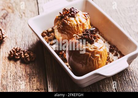 Mele cotte al forno con avena integrale, noci tritate, sciroppo d'acero su tavola di legno, dolce vegano d'autunno e d'inverno, primo piano Foto Stock