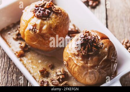 Mele cotte al forno con avena integrale, noci tritate, sciroppo d'acero su tavola di legno, dolce vegano d'autunno e d'inverno, primo piano Foto Stock