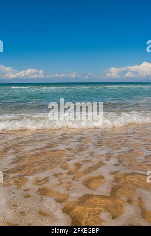 Immagine verticale di onde blu oceaniche strisciate delicatamente al riva in una giornata tranquilla Foto Stock