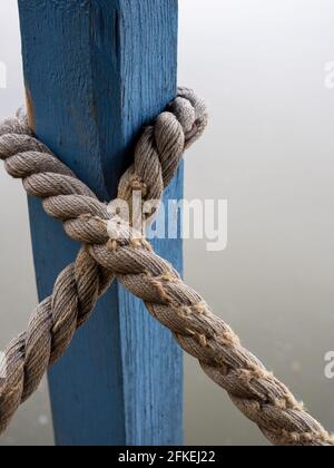 Scatto verticale di una corda legata intorno ad un legno blu colonna Foto Stock