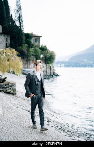 Groom passeggiate lungo il argine della città di Varenna Sul Lago di Como sullo sfondo di vecchi edifici e. montagne Foto Stock