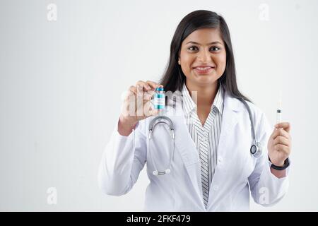 Ritratto di felice eccitato giovane medico indiano mostrando fiala di vaccino contro il coronavirus e la siringa Foto Stock