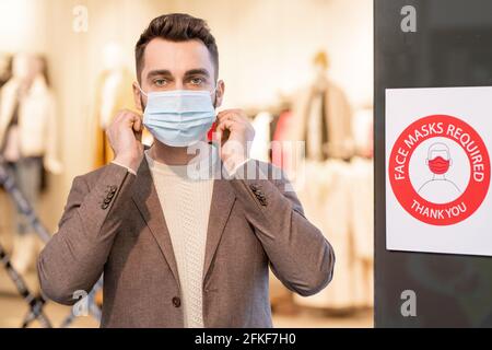 Giovane uomo che indossa una maschera durante lo shopping Foto Stock