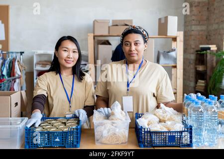 Due giovani donne volontarie in piedi a tavola con cibo libero in scatole di plastica Foto Stock