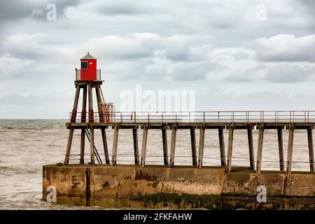 Una giornata molto ventosa sul molo Whitby, nello Yorkshire del Nord, Inghilterra. Whitby è una città storica con le sue strade stravaganti, i negozi e le rovine dell'abbazia. Foto Stock