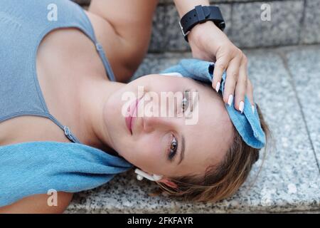 Abbastanza sorridente sfinito giovane sportiva strofinando il sudore da lei fronte quando si riposa all'aperto dopo un allenamento intenso Foto Stock