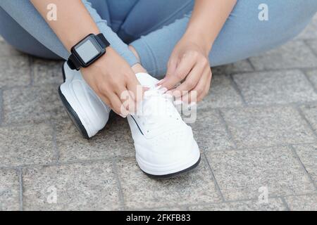 Immagine ravvicinata di una donna sportiva con smartwatch sulla sua legatura al polso scarpe e preparazione per l'allenamento Foto Stock