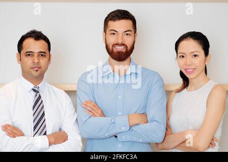 Multi-etnico fiducioso team aziendale di successo che attraversa le armi e lo sguardo fotocamera Foto Stock