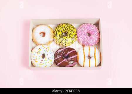 Scatola di ciambelle. Un set o un assortimento di ciambelle colorate smaltate con spruzzette e condimento. Sfondo rosa. Delizioso spuntino o dessert. Foto Stock