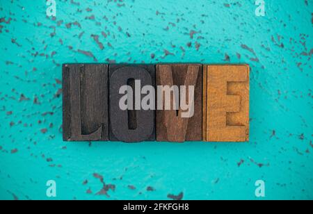 Amore scritto in legno tipo Imposta lettere di blocco su a. Sfondo turchese Foto Stock