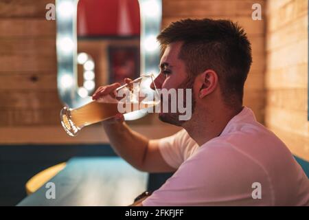 Vista laterale di un giovane maschio europeo che beve birra in il pub Foto Stock