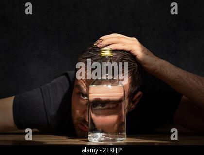 Dipendenza Alcoloica. Un bell'uomo con barba e baffi trattiene bevande alcoliche sullo spazio di copia scuro. Ragazzo con una bottiglia di vodka sul tavolo. Foto Stock