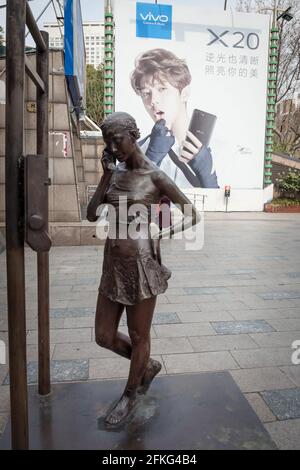 Status di bronzo di giovane ragazza al telefono di fronte pubblicità per un telefono cellulare Foto Stock