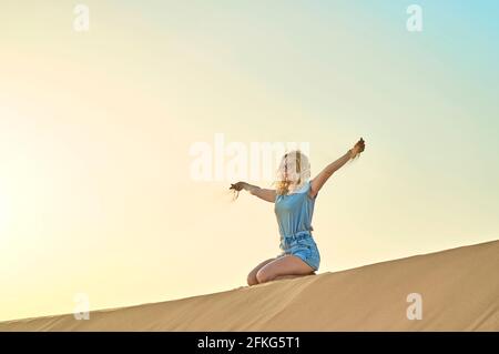 Bella donna brunette in abiti bianchi rilassandosi sulla cima della duna di sabbia nel deserto del Sahara Marocco. Nebbia di mattina prima dell'alba. Armonia con la natura. Foto Stock