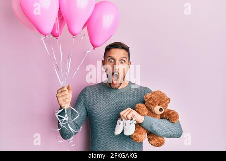 Bell'uomo con barba che si aspetta una bambina che tiene palloncini, scarpe e orsacchiotto orso paura e scioccato con sorpresa e stupito espressione, paura e Foto Stock