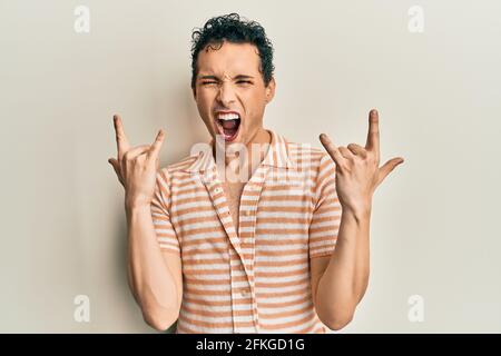 Bell'uomo che indossa una t-shirt casual che grida con l'espressione pazza facendo simbolo rock con le mani in su. Stella della musica. Concetto pesante. Foto Stock