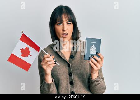 Giovane donna ispanica che detiene bandiera canada e passaporto indistinta e confuso espressione. Dubbio concetto. Foto Stock