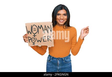 Giovane latino transessuale donna che tiene la bandiera di potere della donna sorridente felice di puntare con mano e dito a lato Foto Stock