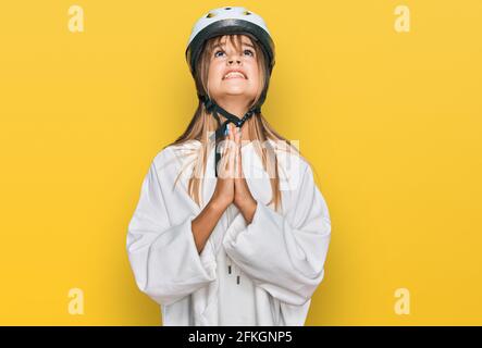 Teenager caucasico ragazza che indossa casco da bici che prega con le mani insieme con espressione di speranza sul viso molto emotivo e preoccupato. Foto Stock