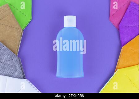 Disinfettante con alcol per le mani e diversi colori FFP2 o N95 maschere facciali respiratori intorno. Su sfondo viola. Vista dall'alto livello piatto. Protezione da covi Foto Stock