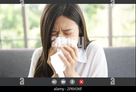 Visualizzazione dell'applicazione dello schermo di una donna asiatica che sta avendo l'influenza e sta starnutendo e videoconferenza. Concetto di tecnologia e salute, telefono online Foto Stock