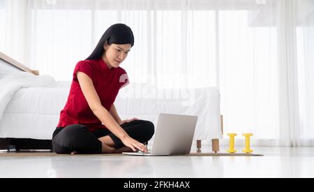 Ritratto della giovane donna asiatica sana che pratica esercizi di yoga seduto in camera da letto e imparare online sul computer portatile a casa. Concetto di esercizio e. Foto Stock