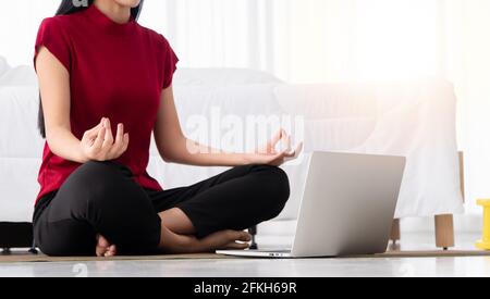 Ritratto della giovane donna asiatica sana che pratica esercizi di yoga seduto in camera da letto e imparare online sul computer portatile a casa. Concetto di esercizio e. Foto Stock