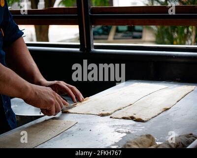 Le mani della donna tagliano un po' di pasta di farina sul tavolo di metallo Foto Stock