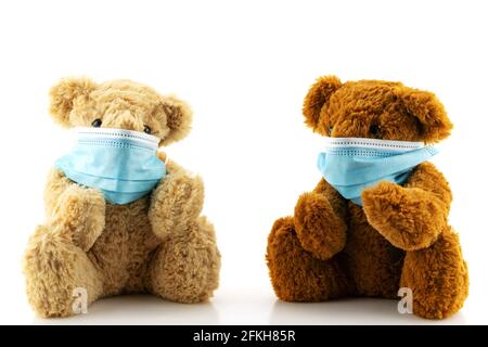 Due orsacchiotti che indossano una maschera protettiva, l'orso Teddy sono seduti in maschere mediche blu su sfondo bianco, concetto di protezione dal disfatto respiratorio Foto Stock