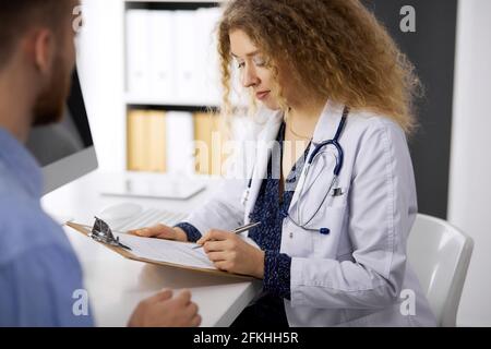 Medico femminile e paziente-uomo che discutono l'esame di salute corrente mentre si siede in clinica. Servizio medico perfetto e concetto di medicina Foto Stock