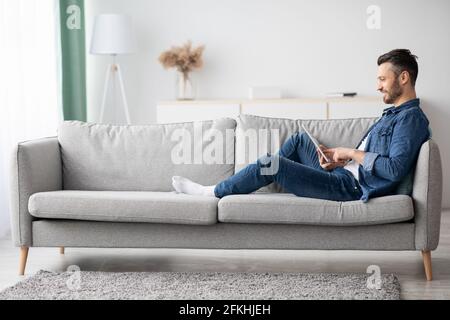 Bell'uomo con la bearded che usa il tablet digitale a casa Foto Stock