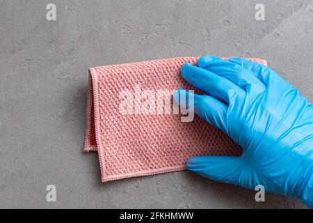 Pulizia della casa. Una mano in un guanto di lattice blu sta sfregando un panno di microfibra rosa su una superficie di intonaco grigio, primo piano. Foto Stock