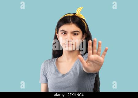 Seria ragazza teen indiana che gesturing STOP su sfondo studio blu. Concetto di opinione negativa Foto Stock