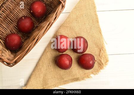 Alcune prugne rosse fresche, succose, biologiche, in un cesto di vite e con un zaffetto di iuta, su un tavolo di legno, primo piano, vista dall'alto. Foto Stock