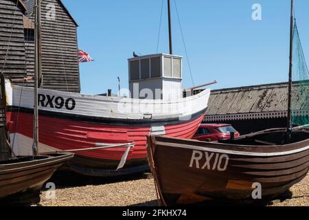 Idea di staycation. Vecchie barche da pesca in legno in barca e in mostra allo Stade, Hastings. NET Shops e bandiera britannica in background. East Sussex, Regno Unito Foto Stock