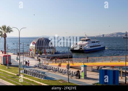 Goztepe, Izmir - Turchia- 04-22-2021: Un traghetto si avvicina al molo dei traghetti di Goztepe. Le persone in spiaggia sono in bicicletta o a piedi. Foto Stock