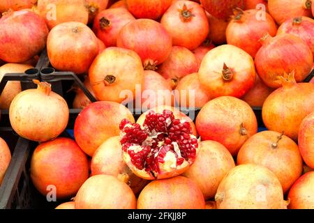 Mucchio di melograni organici maturi rossi, interi e dimezzati, accatastati piacevolmente al mercato agricolo locale di produzione. Frutta succosa piena di vitamine, vegan sano Foto Stock