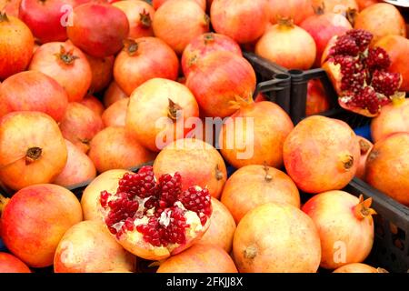 Mucchio di melograni organici maturi rossi, interi e dimezzati, accatastati piacevolmente al mercato agricolo locale di produzione. Frutta succosa piena di vitamine, vegan sano Foto Stock