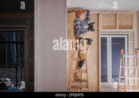 Caucasico Construction Worker nei suoi anni '40 Installazione di elementi Drywall soffitto nel recentemente sviluppo residenziale Skeleton telaio in legno Made Building. Foto Stock